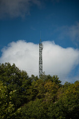 Una antena de telecomunicaciones asomandose en la naturaleza ante un cielo azul con nubes