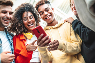 Young people using smart mobile phone device outdoors - Happy teenagers having fun together watching video stories on social media platform - Trendy technology and youth lifestyle concept