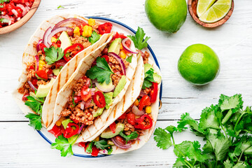 Mexican cuisine. Tacos with beef, corn, red beans, tomato salsa sauce and onions in corn tortilla on plate. White table background, top view