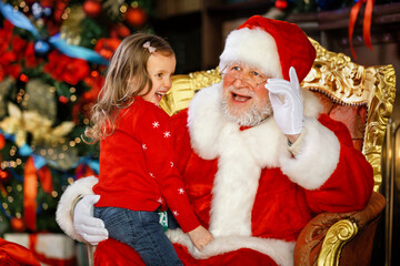 Santa Claus tells a funny story to a cute little girl on the holiday of Christmas.