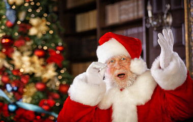 A portrait of a very surprised Santa Claus in a beautiful room next to a Christmas tree looks right into the frame.
