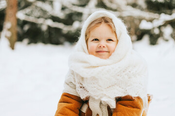 portrait cute little girl toddler in white russian style orenburg down shawl scarf in snow winter forest, concept of Christmas holidays and New Year in retro vintage style