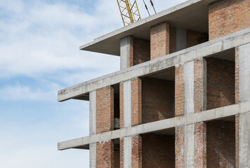 Part of an unfinished red brick building and a construction crane against the sky