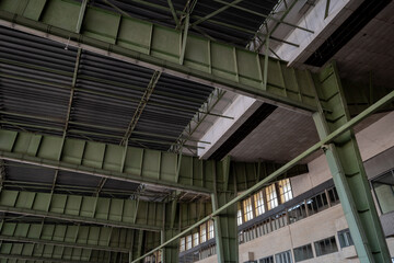 View under high ceiling of open interior space with huge steel truss, columns and beam structure building at former airport terminal in Berlin,  Germany.