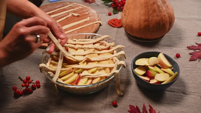 Close-up. Step-by-step making a crusty lattice pattern from striped pastry dough, on top of American classic apple pie with pumpkin for Thanksgiving Day. Fresh ingredients on the kitchen table.