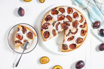 Homemade delicious plum tart with with sugar powder on white wooden table. Top