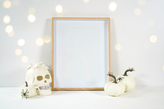 Halloween product mockup. Wall art picture frame mockup with white skull pumpkins against a white background with bokeh party lights. Negative copy space.