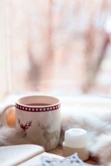 christmas still life. cup of coffee, open book, white blanket, candle, handmade snowflake on windowstill near light window, selective focus