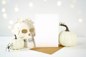Halloween product mockup. Blank 5x7 greeting card or party invitation with white skull pumpkins against a white background with bokeh party lights. Negative copy space.