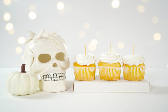 Halloween product mockup. Party treats cupcakes with white skull pumpkins against a white background with bokeh party lights. Negative copy space.