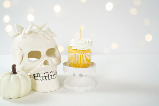 Halloween product mockup. Party treats cupcakes with white skull pumpkins against a white background with bokeh party lights. Negative copy space.