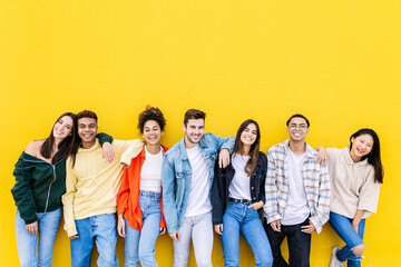 Young adult united group of multiracial happy friends leaning on yellow wall - Community and unity concept with diverse trendy teenage people smiling at camera - Powered by Adobe