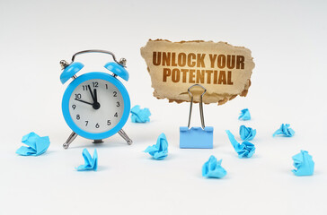 On a white surface there is an alarm clock, crumpled paper and a cardboard sign with the text -...