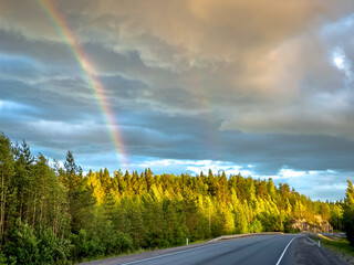 Asphalt road under the clouds. Top view of the road through the green summer forest. Rainbow over the forest in Karelia