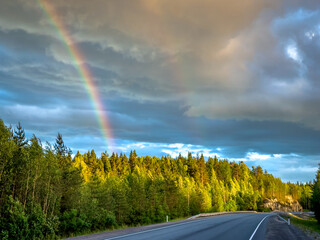 Asphalt road under the clouds. Top view of the road through the green summer forest. Rainbow over the forest in Karelia