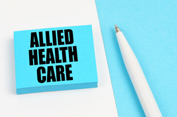 On a white and blue surface, a pen and blue stickers with the inscription - Allied Health Care