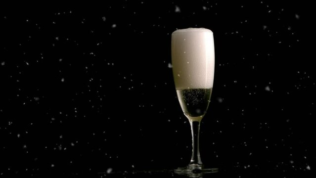 Animation of snow falling over glass of champagne