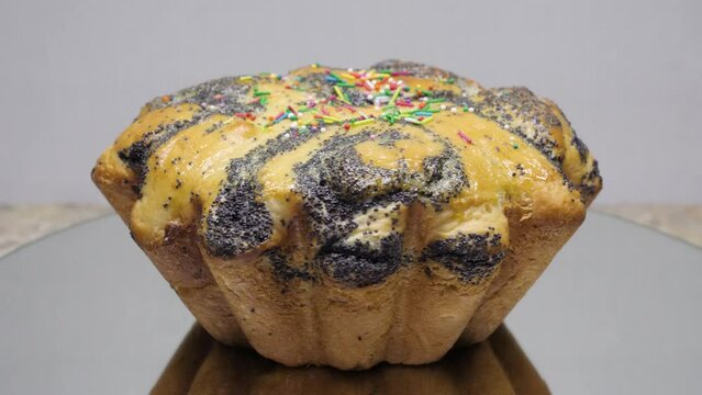 Closeup sweet yellow Easter cupcake with poppy seeds decorated with colorful sprinkles rotates on mirror background, 4K