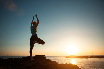Fototapeta na wymiar A woman does gymnastic yoga at sunset on the ocean.