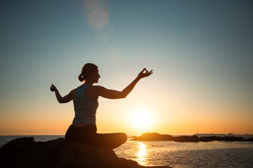 Yoga woman meditating in the lotus position during sunset on the oceanfront.