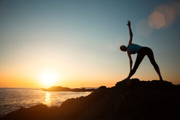 Silhouette of a woman doing gymnastics exercises during sunset on the ocean.