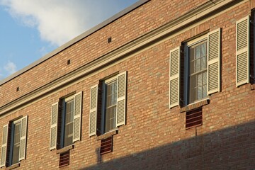 Fototapeta na wymiar Brick apartment building roof line windows shutters in afternoon sun
