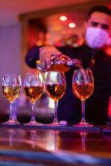 Adult man wearing face mask pouring red wine into the wineglasses