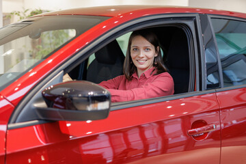 happy woman buys a red car at a car dealership. signing a trade-in contract and handing over keys, shaking hands. A successful woman chooses a new car. Rent a vehicle or repair service center.