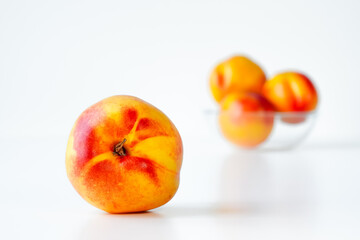 Nectarine close-up on white background, space for text. Ripe bright nectarine fruit in foreground, several nectarines of the same variety in blurred background, copy space, at eye level.
