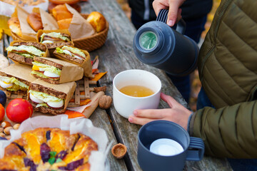 picnic in the autumn season, food on a wooden table, hot tea, pastries and sandwiches