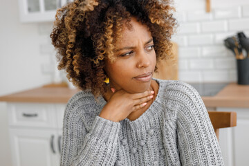 African American woman with a cold and sore throat drinks vitamins and measures body temperature....