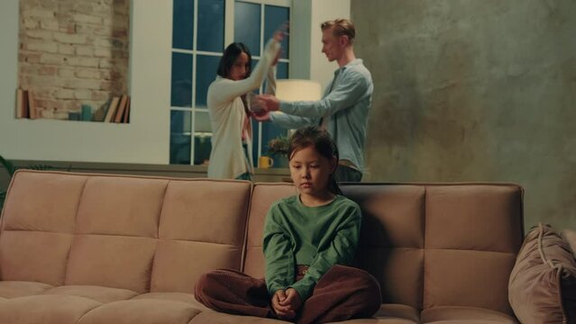 Multiracial parents arguing at home at night. Frightened child closes his ears.