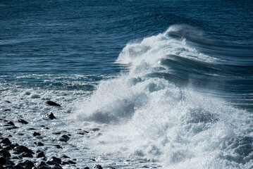 Naklejka premium Full frame shot of the deep blue Atlantic Ocean and a beautiful wave crashing on the coast of Paul do Mar, a popular surf spot on Madeira island, Portugal