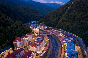 Sochi, Russia - August 06 2020: Night panorama of the Mzymta river embankment at the Rosa Khutor ski resort. Evening illumination of hotels and infrastructure