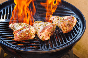 Raw traditional barbecue lamb shank grilled as close-up on a charcoal grill with fire and smoke