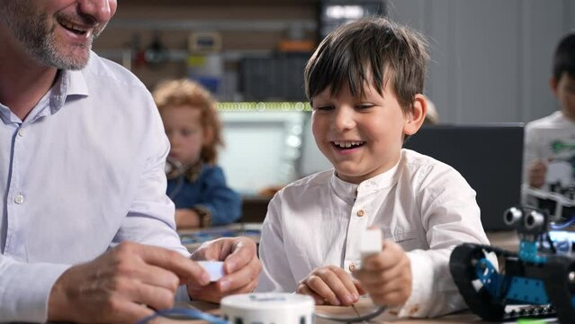 Close up excited elementary school boy smiling and having fun while testing robotics he made in class. Brilliant boy building and programming electric toys at elementary school robotics classroom.