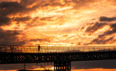 Solo person walkin on a bridge with a burning colorful sky on background