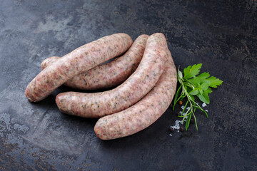 Rohe grobe Allgäuer Bratwurst garniert mit Kräutern und Gewürzen als close-up auf rustikalen...