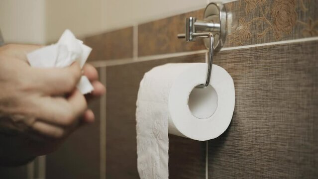 A man uses a roll of toilet paper. Unwinds it. Close-up.