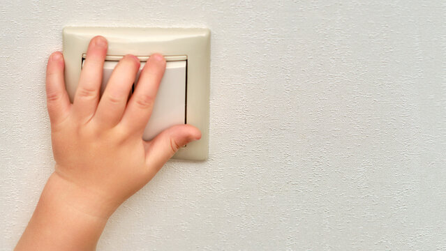 Child S Hand Presses The Light Switch, Copy Space. Toddler Baby Boy Turns On The Lamp In The Room. Kid Aged One Year And Three Months