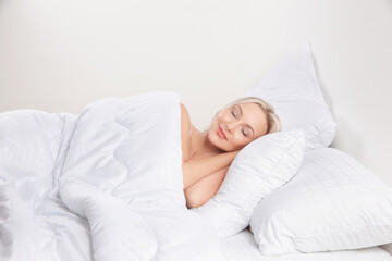 blonde girl in bed with white pillows and a blanket in a bright bedroom, home textiles