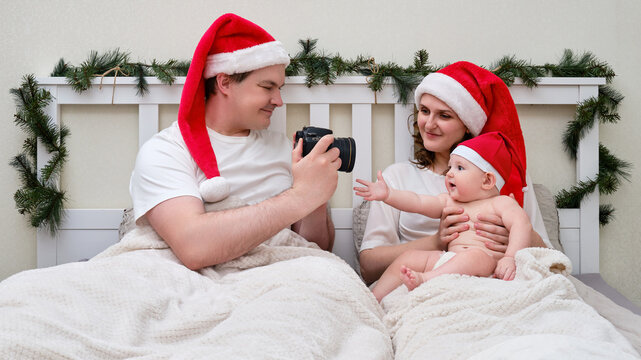 Happy Man And Woman With Child Take Photo Camera In Bed Decorated For Christmas And New Year, Family Couple In Home Bedroom