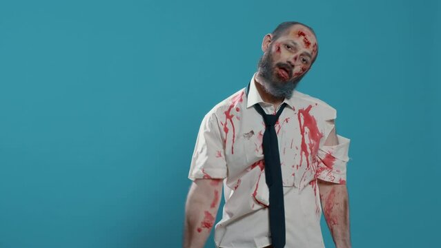 Creepy zombie with deep and bloody scars standing on blue background. Mindless looking brain dead crazy monster acting bizarre while growling sinister and spooky at camera. Studio shot