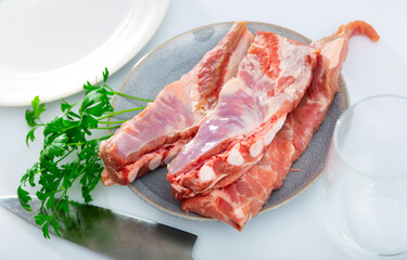 Raw meaty pork ribs slabs on plate with fresh greens ready for cooking ..