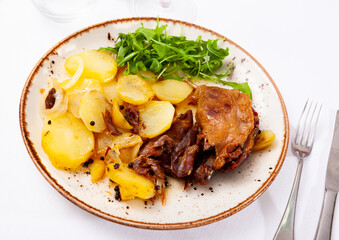 Traditional french food, duck confit with stew potatoes and greens on a plate in a cafe