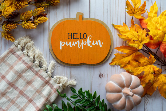 Flat lay background for fall and autum, with maple leaves, foliage, pumpkins and a plaid towel or blanket, with Hello Pumpkin