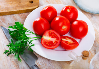 Fresh red tomatoes on wooden table with kitchen knife and bunch of parsley.