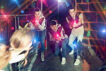 Joyful people aiming laser guns at other players during lasertag game in dark room