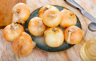 Image of whole onion bulbs on a wooden table next to olive oil and a salt shaker. Ingredients for cooking
