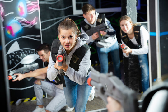 Portrait of excited woman holding laser gun in arena, playing laser tag game with friends. High quality photo